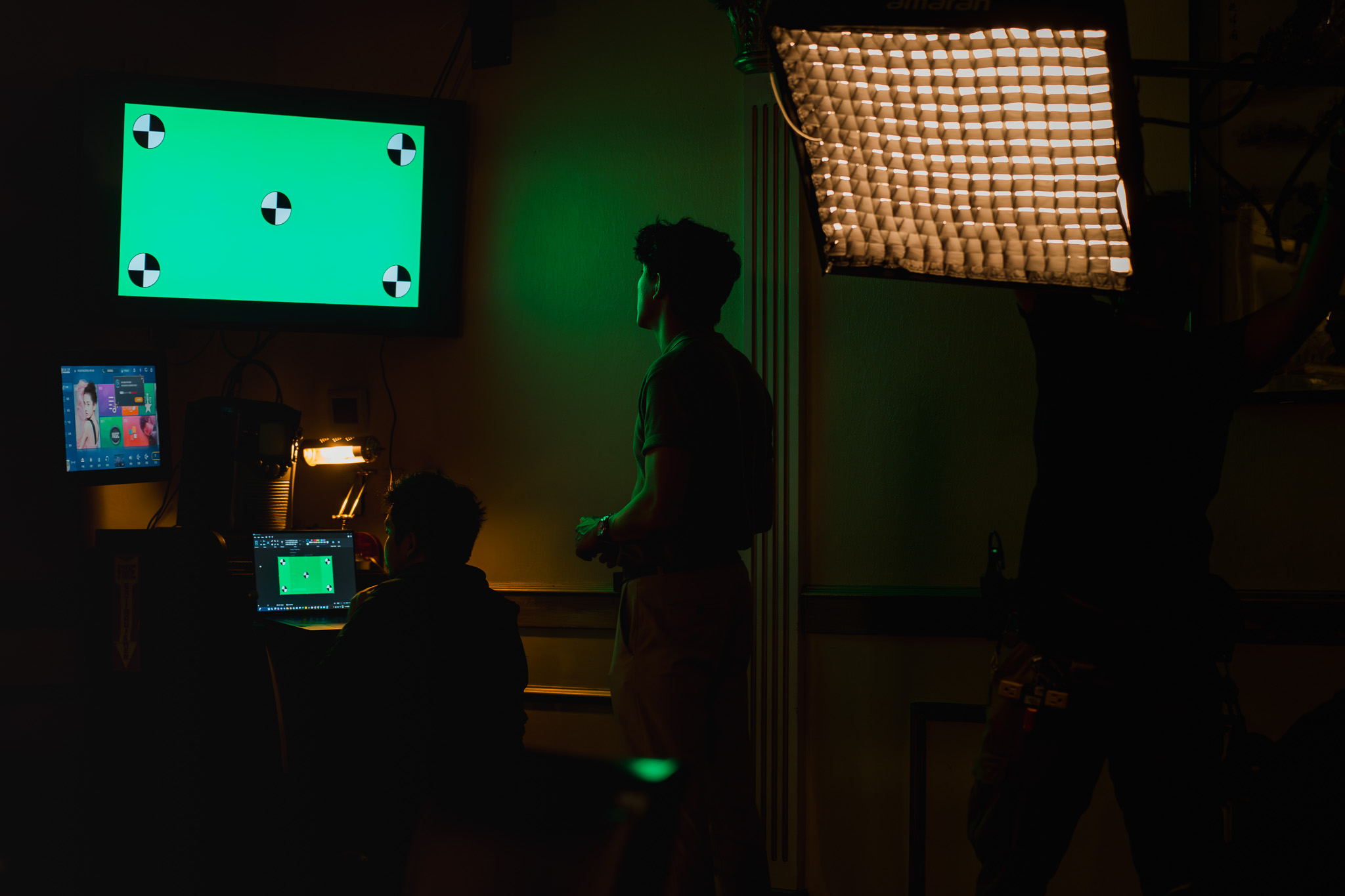 A crew member watches a green-screen monitor on set, with a softbox light overhead